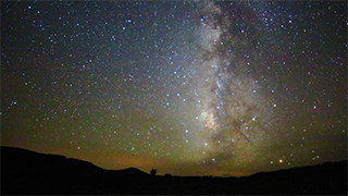 An image of the Milky Way Galaxy at night, with rocks in silhouette in the foreground.
