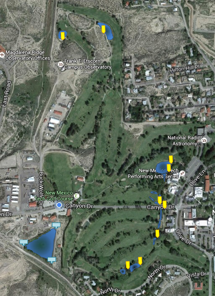 Aerial image of the New Mexico Tech Golf Course, Etscorn Campus Observatory, and the Facilities Management-hosted fishing pond. The Golf Course is divided in the middle of the image by Canyon Road, which leads to Facilities Management. Yellow arrows are shown on the image at each Golf Course water hazard, signifying that fishing is not allowed in these locations. At the bottom left of the image (the southwestern corner of the image) is a triangular pond with blue sign images, signifying that this pond is available for people interested in fishing on campus.