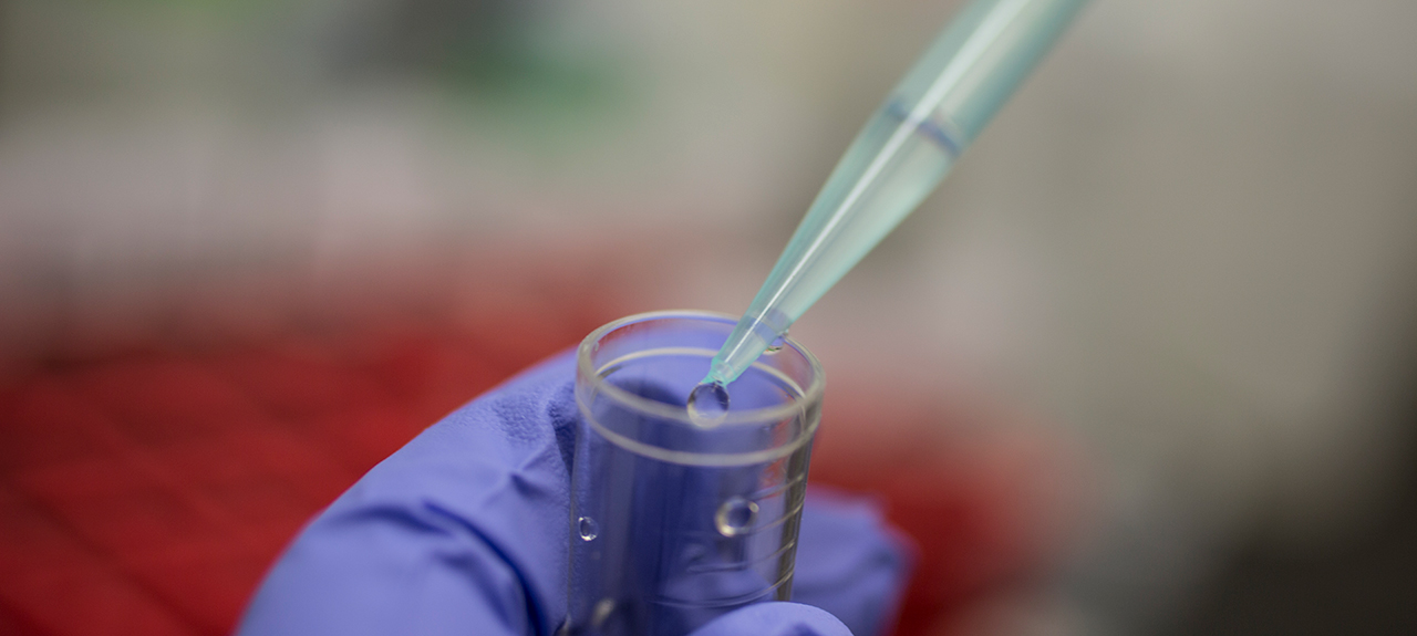 Close up image of liquid being dropped into a test-tube with a pipette.