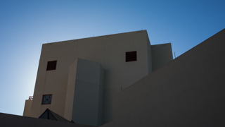 A close up image of Workman Center, looking up. The sun is behind the building and the sky above the building is cloudless and light blue.
