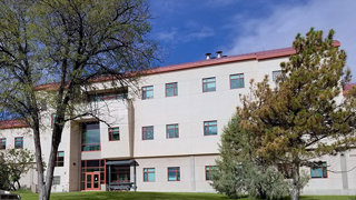 An exterior photo of the Jones Hall Annex building. Trees can be seen in the foreground, while blue sky and clouds are visible past the building.