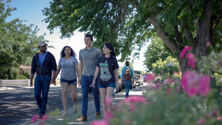 An image of students walking on campus. Out of focus flowers can be seen in the image's foreground.