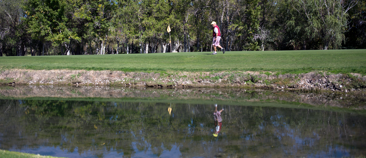 Hero image of man walking towards the golf flag, with a water hazard in the foreground.